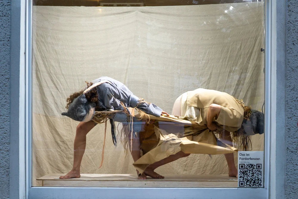 Two performers with animal masks and paper costumes in the Forderfenster